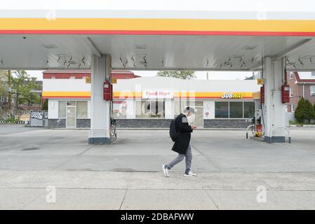 Ein Mann, der eine Maske trägt, kommt an einer leeren Tankstelle am Northern Boulevard in Sunnyside, Queens, vorbei. Stockfoto