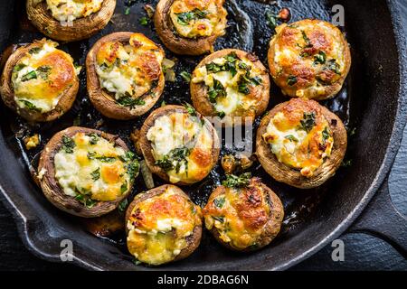 Gebackene Champignons, gefüllt mit Käse, Petersilie und geröstetem Knoblauch in schwarzer Schüssel. Selektiver Fokus. Gesundes Essen Konzept. Stockfoto