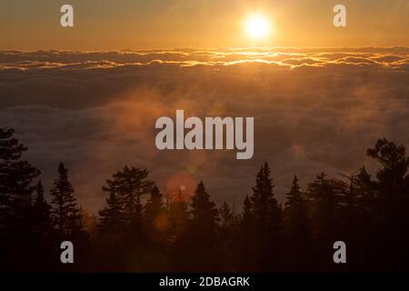 Die Sonne sieht aus wie ein leuchtender orangefarbener Feuerball Als es den Nebel und Nebel über einem erhellt Dicke Wolkenschicht, die das Tal am Sandia bedeckt Moun Stockfoto