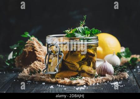Muscheln aus der Dose in Olivenöl und Zitronensaft mit Gewürzen, Knoblauch und Kräutern, schwarzer Küchentisch aus Holz, selektiver Fokus Stockfoto