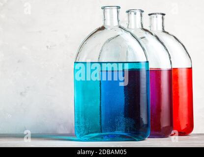 Glasflaschen mit Farbtintenlösungen auf grauer Holzplatte in der Nähe von grauer Betonwand Stockfoto