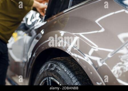 Der Spezialist trägt Schutzfolie auf die Fahrzeugoberfläche auf. Installation der Beschichtung, die die Farbe des Automobils vor Kratzern schützt. Neues Fahrzeug in der Garage Stockfoto