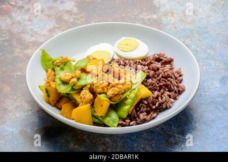 Pfannengerichte Zuckerschoten mit Kürbis und Huhn, serviert mit braunem Reis und gekochtem Ei Stockfoto