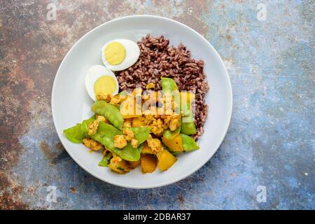 Pfannengerichte Zuckerschoten mit Kürbis und Huhn, serviert mit braunem Reis und gekochtem Ei Stockfoto