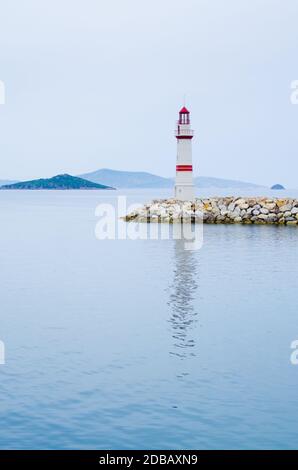 Leuchtturm auf einer Steinstraße in der Mitte des ruhigen Meeres mit Blick auf Berge und Nebel, Turgutreis Türkei Stockfoto