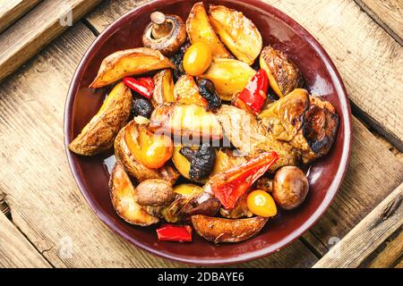 Gebackene hausgemachte Kartoffeln mit Champignonpilzen. Bratkartoffeln auf einem hölzernen Vintage Hintergrund. Stockfoto