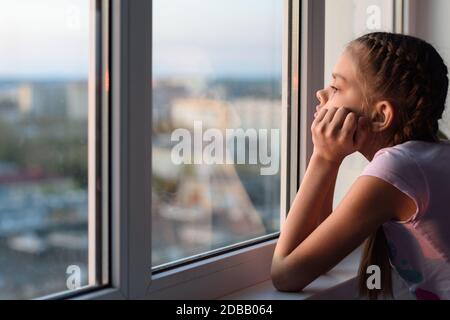 Das Mädchen in Selbstisolation schaut aus dem Fenster Stockfoto