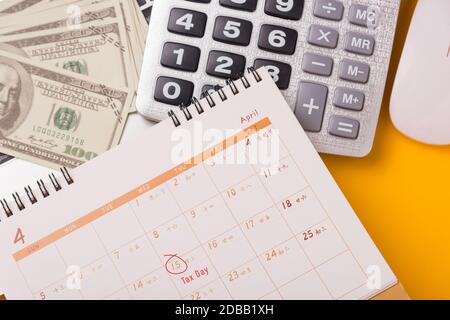 April des Jahres ist Steuertag, Top View flacher Lay-Closeup-Rechner, Laptop, Kalender und Dollar-Geld, auf gelben Hintergrund Business Finance Stockfoto