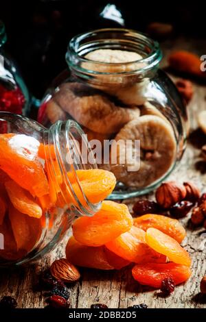 Getrocknete Aprikosen in einem Glas auf dunklem Holzhintergrund mit zerknitterten Nüssen und getrockneten Früchten, selektiver Fokus Stockfoto