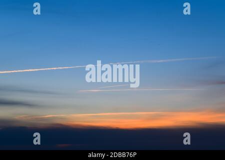 Contrail aus einem Flugzeug auf einem blauen Himmel gegen einen Sonnenuntergang. Stockfoto