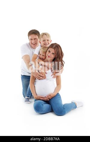Freundliche Familie. Ehemann mit zwei Söhnen lächeln und umarmen schwangere Frau, isoliert auf einem weißen Hintergrund. Glückliche Eltern. Schwangere Mutter und f Stockfoto