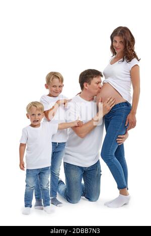 Freundliche Familie. Ehemann mit zwei Söhnen lächeln und umarmen schwangere Frau, isoliert auf einem weißen Hintergrund. Glückliche Eltern. Schwangere Mutter und f Stockfoto