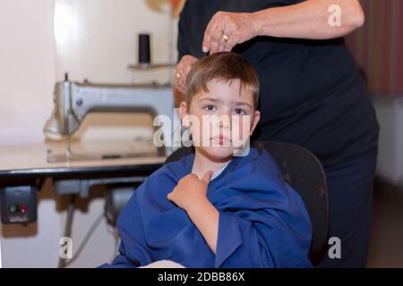 Großmutter schneidet Haare zu seinem kleinen Enkel in ihrem Hause Nähzimmer. Leben zu Hause während Lockdown. Stockfoto