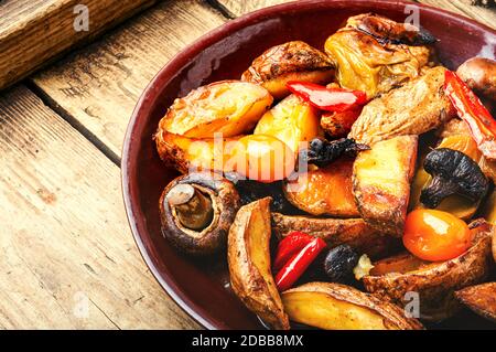 Gebackene hausgemachte Kartoffeln mit Champignonpilzen. Bratkartoffeln auf einem hölzernen Vintage Hintergrund. Stockfoto