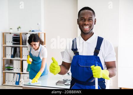 Portrait EINES fröhlichen männlichen Hausmeisters mit Reinigungsgeräten im Büro Stockfoto