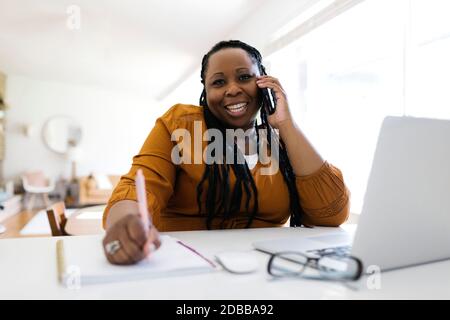 Frau, die am Schreibtisch telefoniert, während sie von zu Hause aus arbeitet Stockfoto