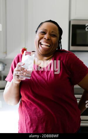 Portrait der lächelnden Frau in lila Kleid hält Glas Wasser Stockfoto
