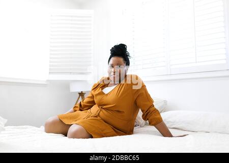 Porträt einer lächelnden Frau in orangefarbenem Kleid auf dem Bett sitzend Stockfoto