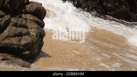 Eine Nahaufnahme des Wassers, das am Mayto Beach in Jalisco, Mexiko, gegen Sand und Felsen krachend ist. Stockfoto
