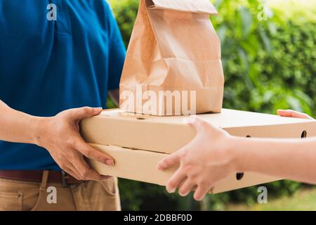 Asiatische Lieferung Express Kurier junger Mann geben Papiertüten Fast Food und Pizza-Box an Frau Kunde erhalten beide Schutzmaske Gesicht, unter Ausgangssperre Stockfoto