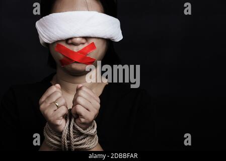 Sklave asiatische Frau Augenbinde wickeln Mund mit rotem Klebeband, gebunden mit Ketten und schloss ihre Augen schwarzen Hintergrund. Freiheit Rede Zensur an Stockfoto