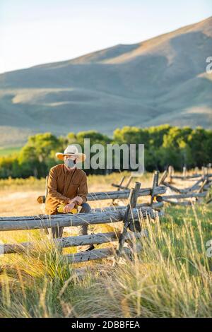 USA, Idaho, Bellevue, Rancher in Gesichtsmaske gegen Zaun auf dem Feld gelehnt Stockfoto