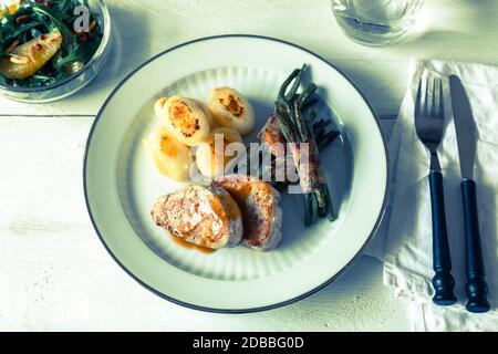 Schweinsmedaillons mit Kartoffeln und Bohnen in Speck gewickelt. Stockfoto