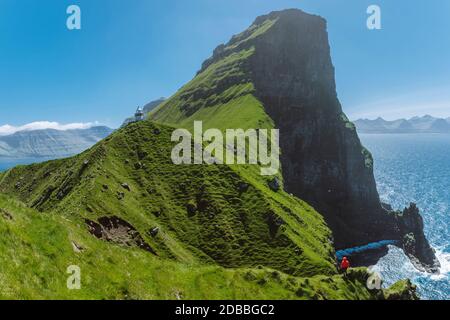 Dänemark, Färöer, Klaksvik, Trollanes, Frau, die auf einer Klippe steht und auf den Kallur Leuchtturm schaut Stockfoto