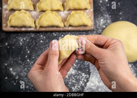 Die Knödel im Mehl auf dem hölzernen Brett, die Hände werden varenik vor dem Kochen modelliert. Top-Ansichten, Nahaufnahme. Stockfoto