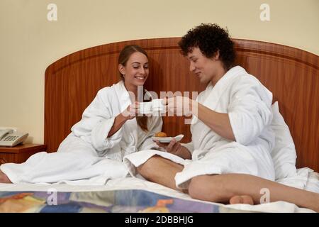 Glückliche junge Familie mit Frühstück liegt im Bett zu Hause. Stockfoto