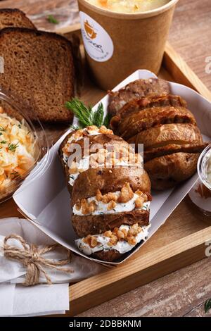 Zitronentee, Salat, Bratkartoffeln mit Fleisch, Sauce und Rosmarin-Wurstbrötchen. Die Gerichte werden mit Einwegutensilien auf einem rustikalen Holztablett serviert. Deli Stockfoto