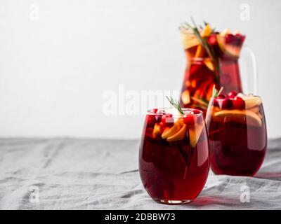 Wintersangria auf Tischplatte mit grauer Leinentischdecke. Juggly von Sangria und Gläser mit Obstscheibe, Cranberry und Rosmarin. Kopieren Sie den Bereich für den tex Stockfoto
