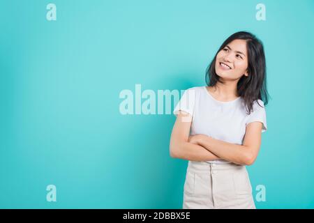 Portrait Asian Beautiful Happy Young Woman Smile tragen weißes T-Shirt, das mit einer Brust steht, die auf einem blauen Hintergrund nach oben blickt Stockfoto