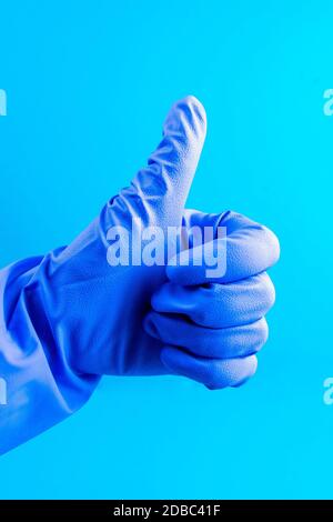 Hand in blauem medizinischen Handschuh zeigt Daumen nach oben. Frauen zeigt Simbol - wie auf blauem Hintergrund. Stockfoto