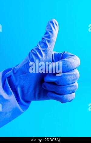 Hand in blauem medizinischen Handschuh zeigt Daumen nach oben. Frauen zeigt Simbol - wie auf blauem Hintergrund. Stockfoto