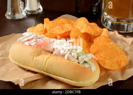 Ein Krabbensalat-Sandwich mit Kartoffelchips an einer Bar Theke mit einem Becher Bier Stockfoto