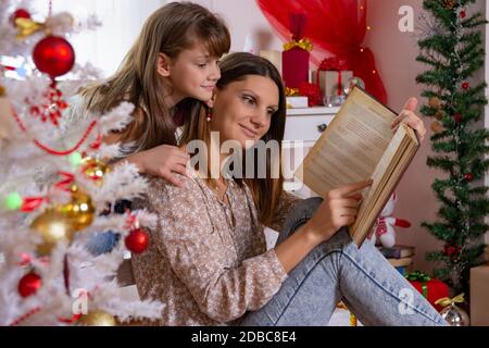 Mutter und Tochter lasen ein Buch in der Nähe eines Weihnachtsbaums Stockfoto
