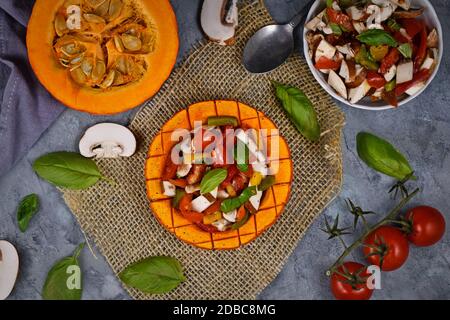 Draufsicht auf vegan gebackenes Red kuri Squashgemüse gefüllt mit Paprika, Tomaten und Pilzen umgeben von Zutaten Stockfoto