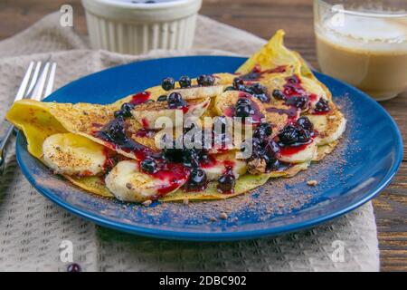 Leckere Pfannkuchen mit Bananen, Heidelbeeren und Honig auf blauem Teller. Nahaufnahme. Hausgemachte Pfannkuchen. Pfannkuchen, Frühstück. Stockfoto