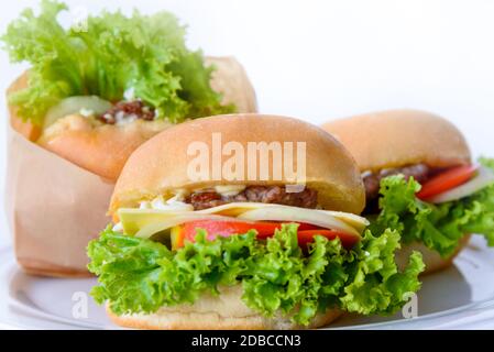 Burger ist ein leckeres amerikanisches Fast Food. Nahaufnahme Gruppe von Set drei Hamburger aus Schweinefleisch oder Rindfleisch, grüner Salat Brot Zwiebel und Tomaten in einem Papier b Stockfoto