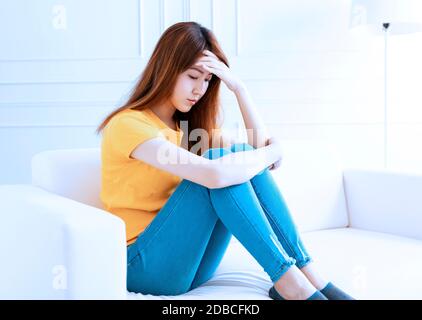 Traurige junge Frau, die zu Hause auf dem Sofa sitzt Stockfoto