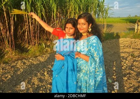 Nahaufnahme von zwei indischen Bengali Mädchen tragen blauen Sari und goldenen Schmuck wie Ohrringe, Halskette, Nasenpins zeigen etwas, selektive Fokussierung Stockfoto