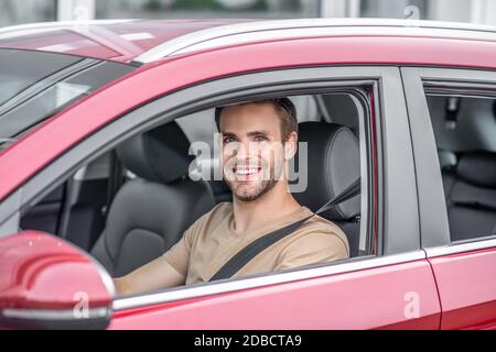 Lächelnder bärtiger junger Mann fährt rotes Auto Stockfoto