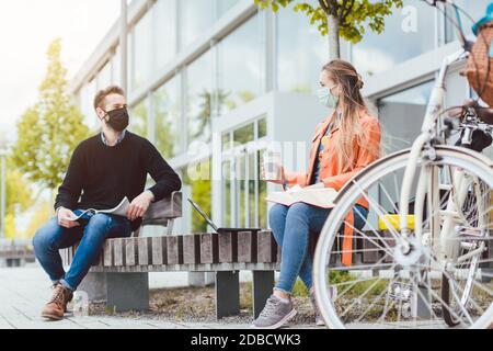 Studenten auf dem Universitätscampus halten soziale Distanz und tragen Gesicht Masken durch Coronavirus Stockfoto