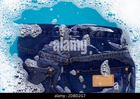 Jeans in Pulver Waschmittel Wasser Auflösung einweichen, waschen Tuch. Wäscheservice Konzept Stockfoto