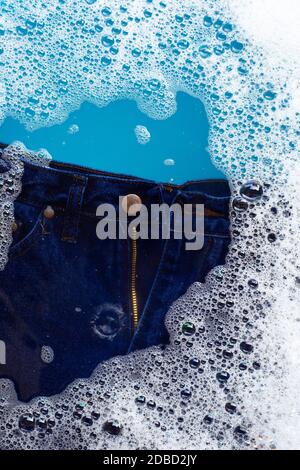 Jeans in Pulver Waschmittel Wasser Auflösung einweichen, waschen Tuch. Wäscheservice Konzept Stockfoto