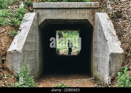 Neugieriger Junge auf dem Fahrrad fährt in einen dunklen Tunnel Unter der Eisenbahn auf dem Land Stockfoto