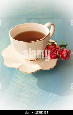 Weiße Tasse Tee und Rosen auf blauem Hintergrund, Jahrgang Stockfoto