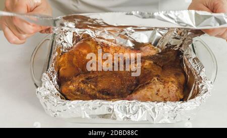 Mariniertes Hähnchenfleisch in einer Glasbackpfanne. Chef wickelt Fleisch mit Aluminiumfolie Stockfoto