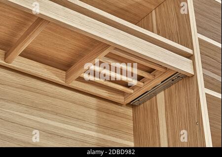 Interne Details der Holzgarderobe mit ausziehbarem Gestell für Kleiderständer. Eiche furnierte Sperrholzschränke mit hellgrau lackierten Schranktüren. Deta Stockfoto